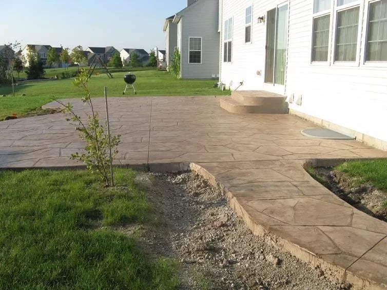 New concrete patio attached to white house with green lawn and landscaping in suburban neighborhood