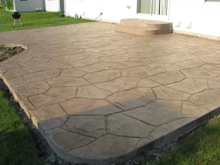 Stamped concrete patio with stone pattern in backyard next to grass and white house